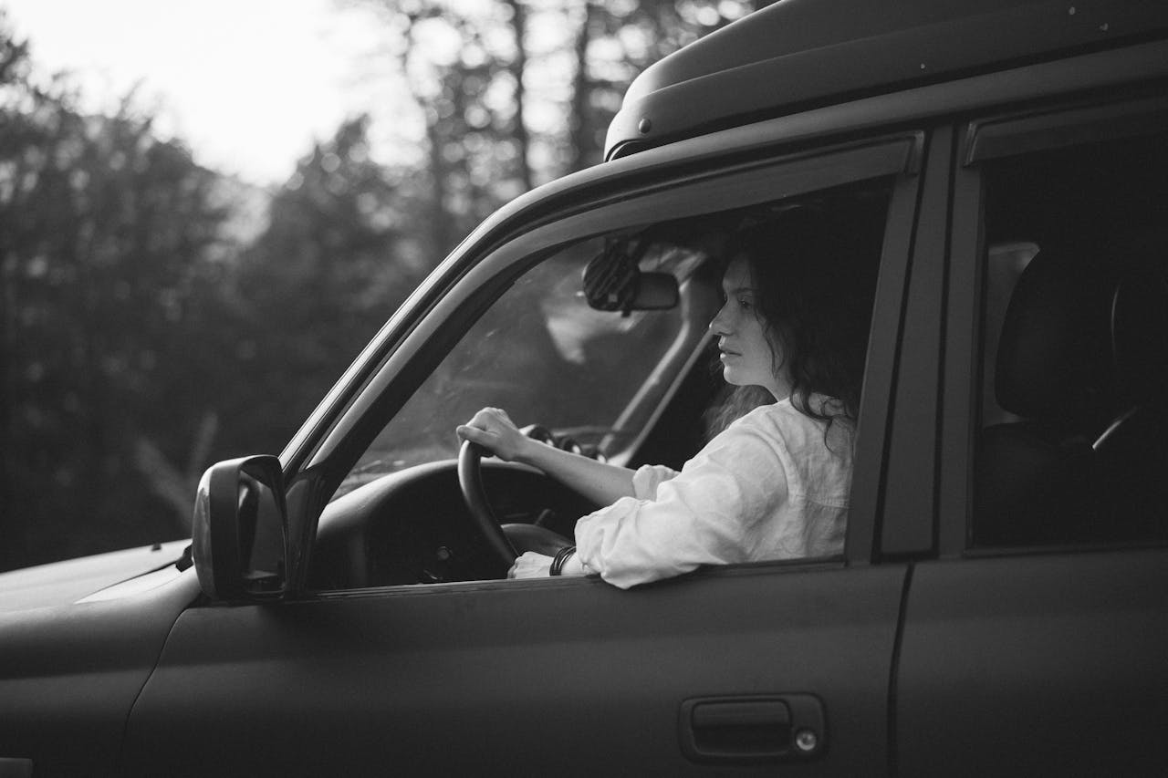 A woman driving a 4x4 vehicle on a scenic road trip in black and white.