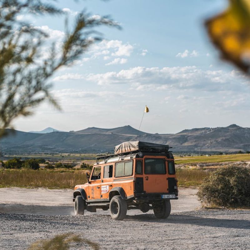 Orange jeep driving through scenic countryside on a sunny day, ideal for adventure or travel themes.