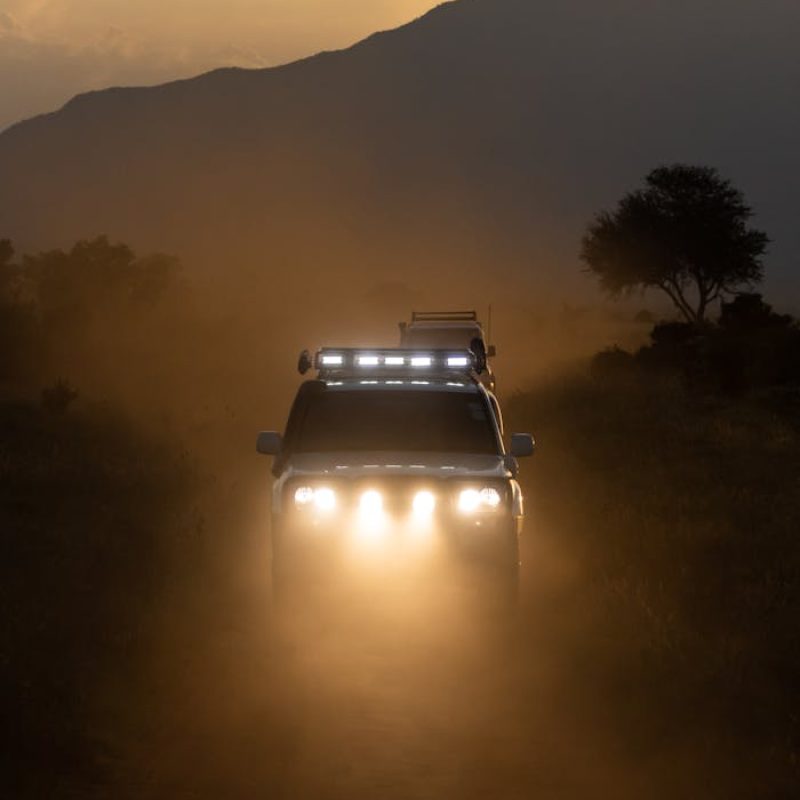 An off-road SUV drives through the dusty savannah of Tsavo, Kenya at sunset.